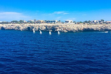 A group of sailboats are in the ocean near a cliff