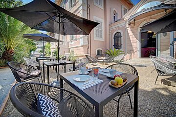 A patio with tables and chairs and umbrellas in front of a pink building