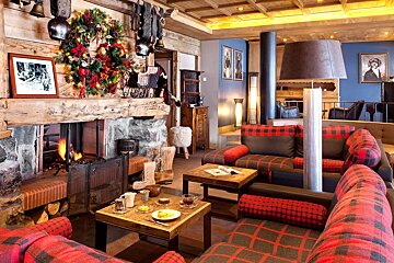 A cozy ski lodge lounge with a roaring fireplace, festive Christmas wreath, and stylish red plaid sofas, exuding rustic warmth.