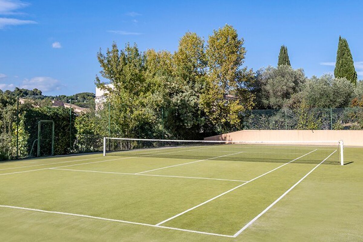 A tennis court is surrounded by trees on a sunny day