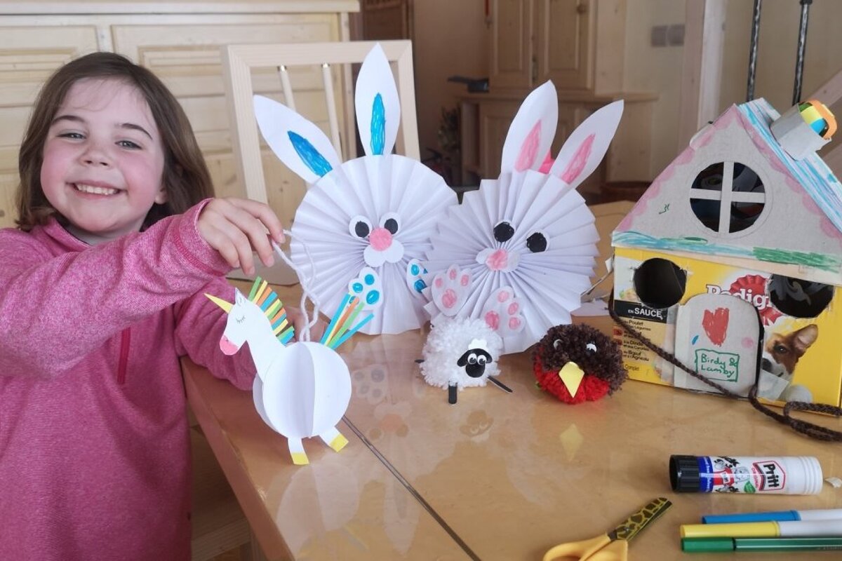 A little girl is making paper animals in front of a box that says fertig