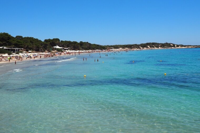 A beach with a lot of people and yellow buoys in the water
