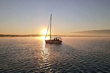 A sailboat is floating in the water at sunset