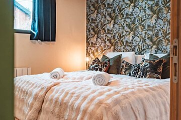 A warm, inviting bedroom features a plush bed with a fluffy white duvet and rolled towels. A tropical leaf accent wall and soft lighting create a cozy ambiance.