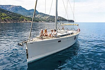 A group of people sit on the deck of a sailboat named vesper