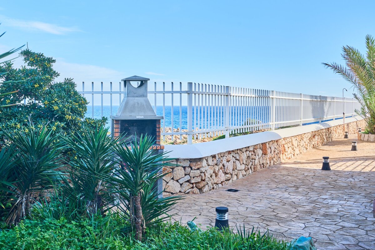 A white fence surrounds a stone wall with a grill in the foreground