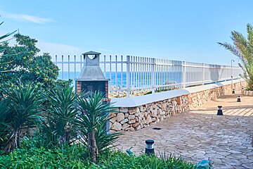 A white fence surrounds a stone wall with a grill in the foreground