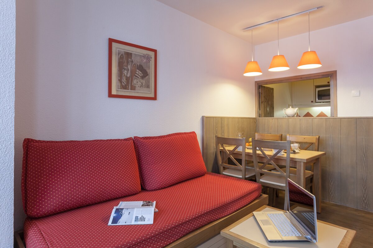 A living room with a red couch and a laptop on a table