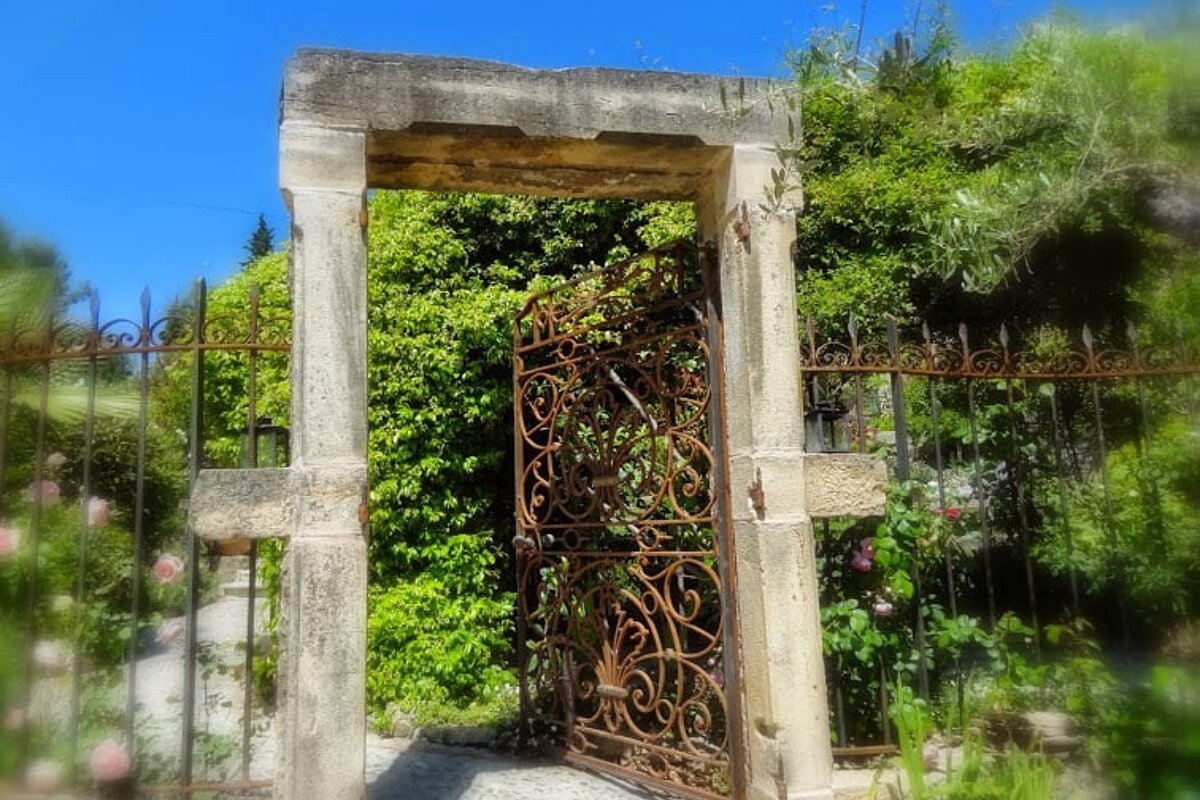 A stone archway with a wrought iron gate leading to a garden