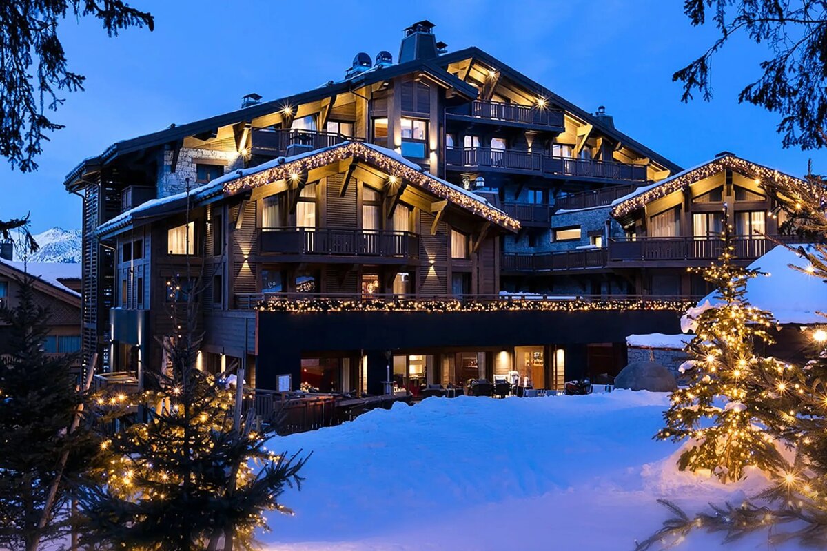 A large, festive mountain chalet covered in snow, sparkling with warm lights against a blue twilight sky.