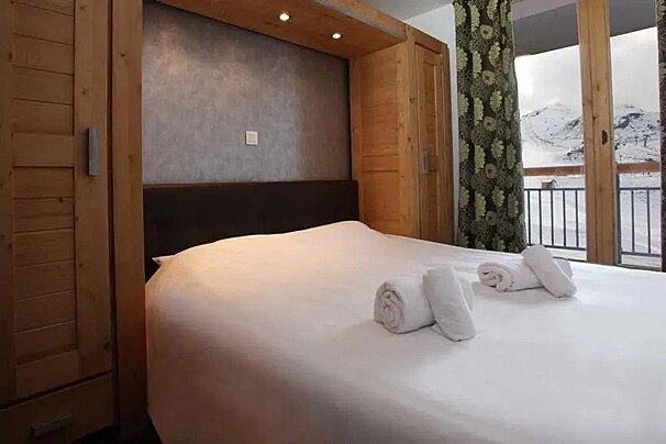 A bedroom with a bed and a balcony with mountains in the background