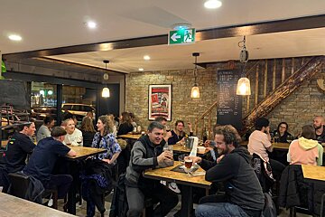A group of people sitting at tables in a restaurant with a green exit sign above them