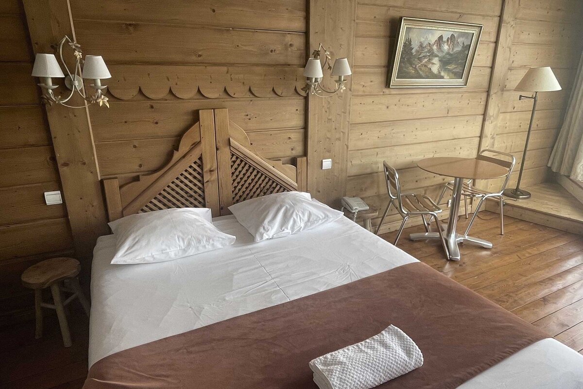A bedroom with a table and chairs and a painting on the wall above the bed