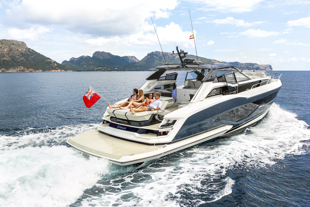 A group of people are sitting on the back of a yacht that says infinity