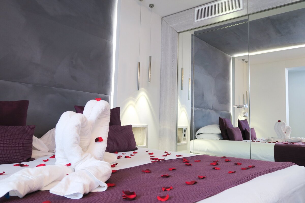 A bed with swans made out of towels and rose petals on it