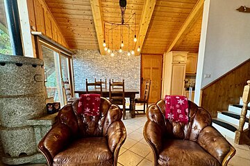 A cozy chalet living area with two brown leather armchairs, festive red snowflake blankets, a stone fireplace, and rustic wood-paneled ceilings.