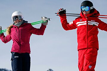 A woman in a colmar jacket holds skis next to a man