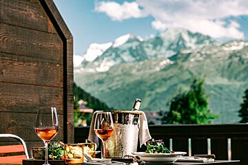 Scenic balcony dining with rosé wine, gourmet food, and a chilled bottle, set against a majestic backdrop of snow-capped mountains.