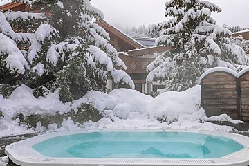 A hot tub is surrounded by snow covered trees