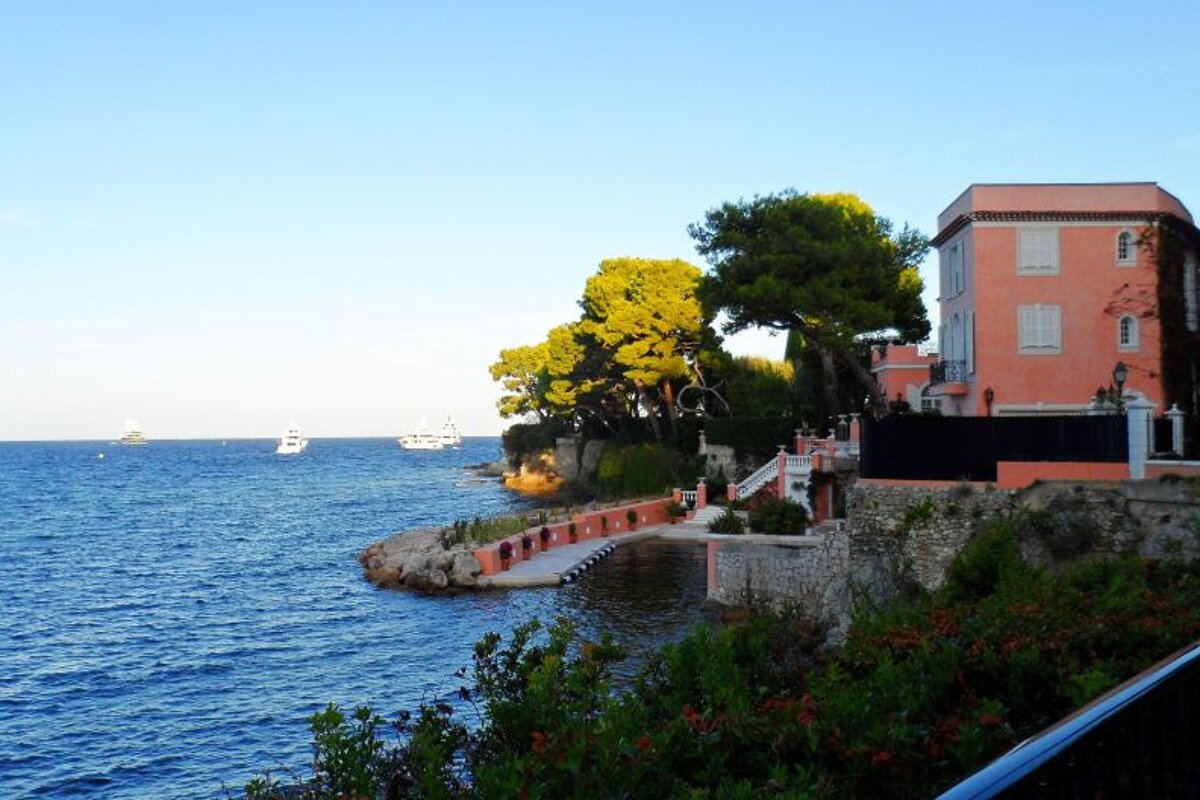 a pink painted house on the edge of the sea with a jetty