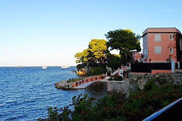 a pink painted house on the edge of the sea with a jetty