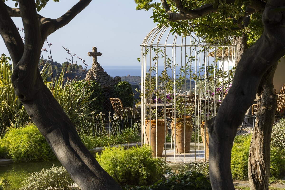 A garden with a bird cage and a cross in the background