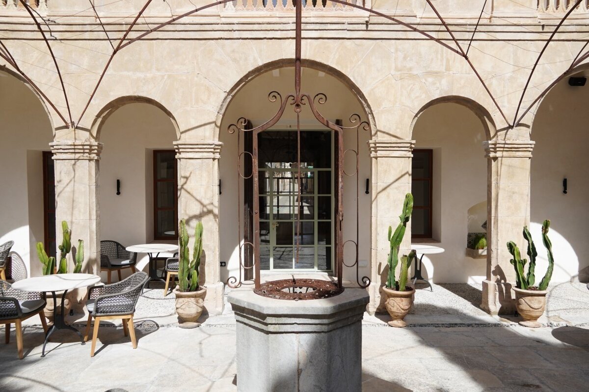 A sunny courtyard with stone arches, a central well, potted cacti, and outdoor seating.