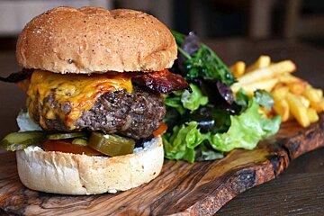 a burger with all the trimmings on a wooden platter