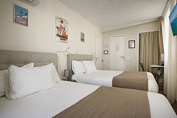 A hotel room with two beds and a cannes poster on the wall