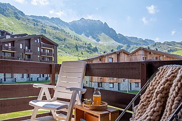 A white chair sits on a balcony with a mountain in the background
