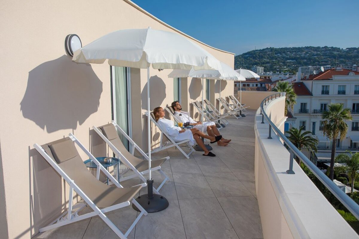 A man and a woman sit on a balcony under white umbrellas