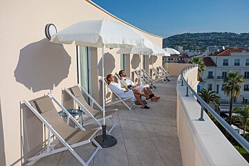 A man and a woman sit on a balcony under white umbrellas