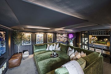 A living room with a green couch and a neon sign that says