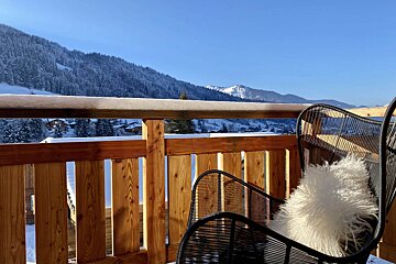 A chair with a white pillow sits on a balcony overlooking snowy mountains
