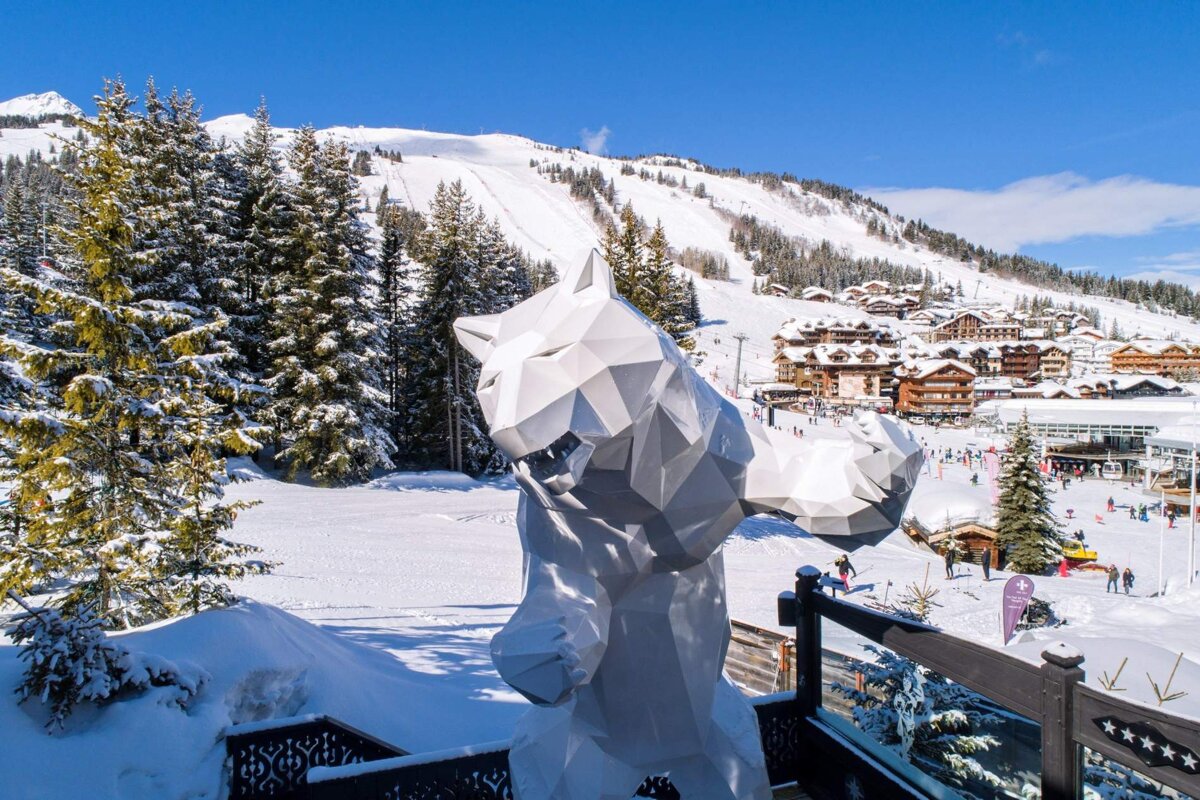 A statue of a wolf stands in front of a snowy mountain