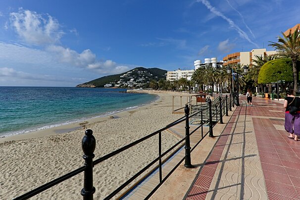 A woman walks down a sidewalk next to a beach