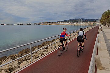 Two people riding bicycles on a path near the water