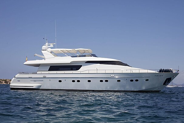 A large white luxury yacht floats on tranquil blue water under a clear, sunny sky, with distant land visible.