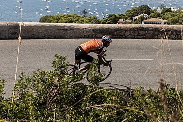 A man is riding a bike down a road with boats in the background