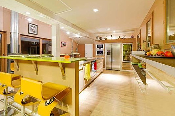 A kitchen with a green counter top , stainless steel appliances , and yellow stools