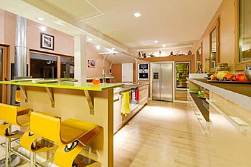 A kitchen with a green counter top , stainless steel appliances , and yellow stools