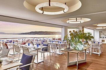 A restaurant with tables and chairs with a view of the ocean