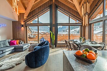 Modern, spacious chalet with vaulted wood ceilings, open-plan living/dining, and huge windows offering stunning snowy mountain views.