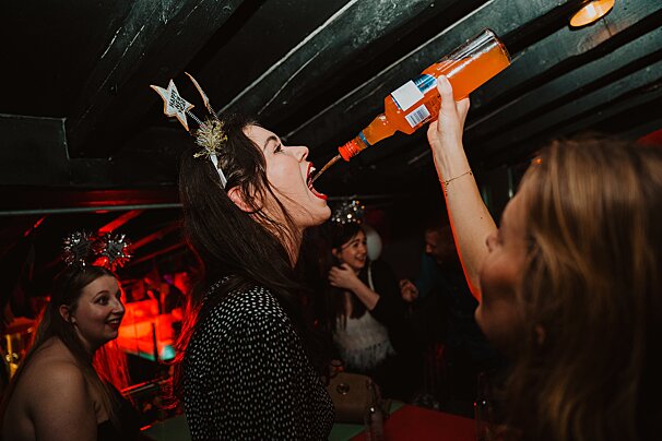 A woman is drinking from a bottle with a label that says ' aperol ' on it