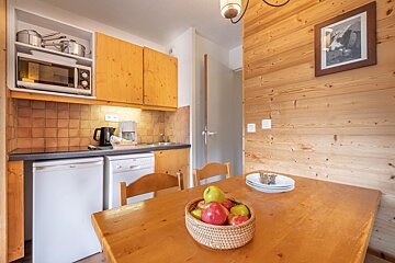 A basket of apples sits on a wooden table in a kitchen