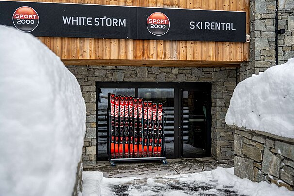 A row of skis are lined up in front of a sport 2000 store