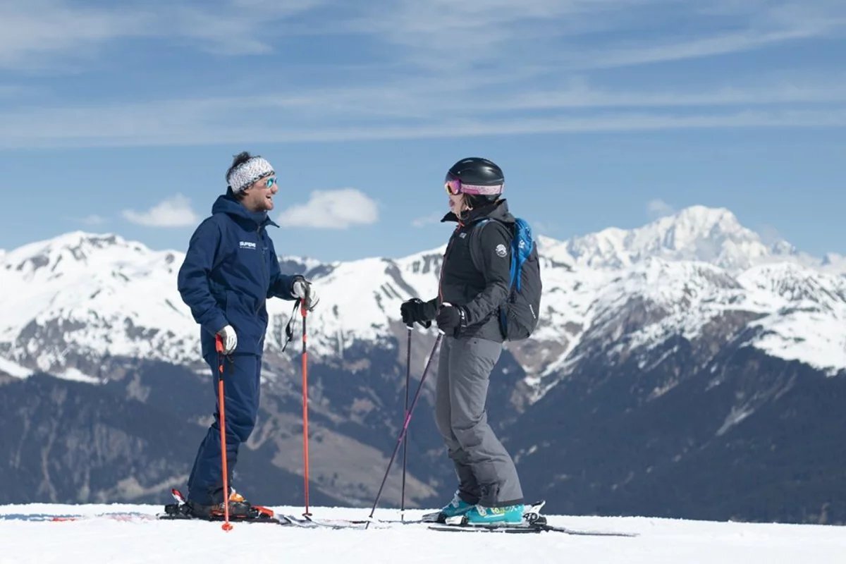 A man wearing a jacket that says uvex talks to a woman on skis