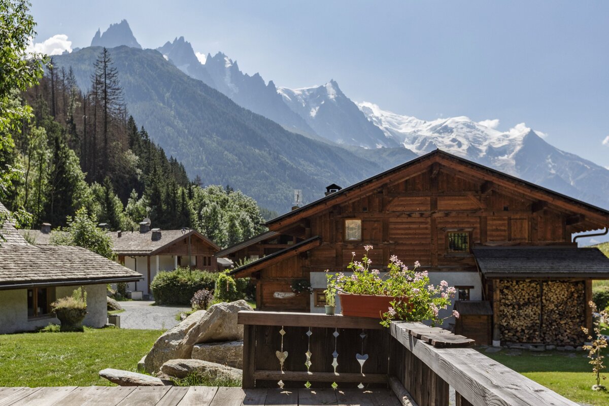 A wooden house with mountains in the background and a planter of flowers on the porch