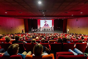 A large auditorium filled with people watching a presentation