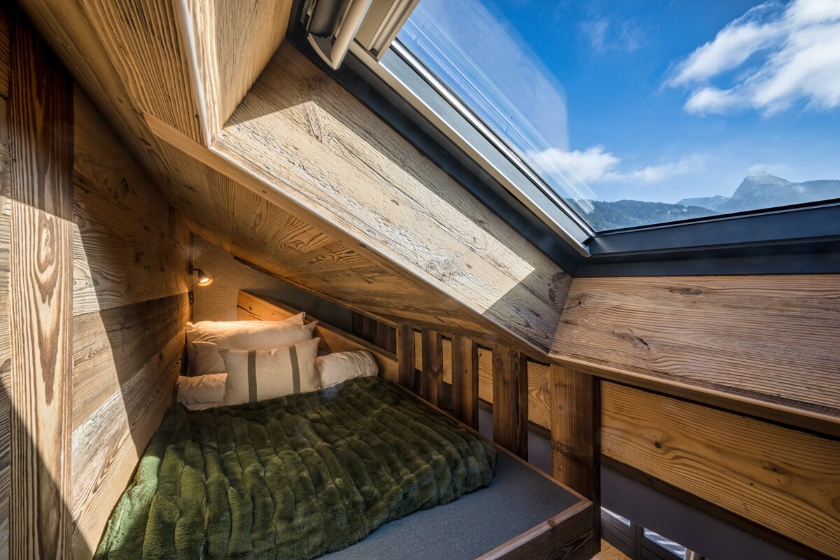 A bed with a green blanket sits under a skylight